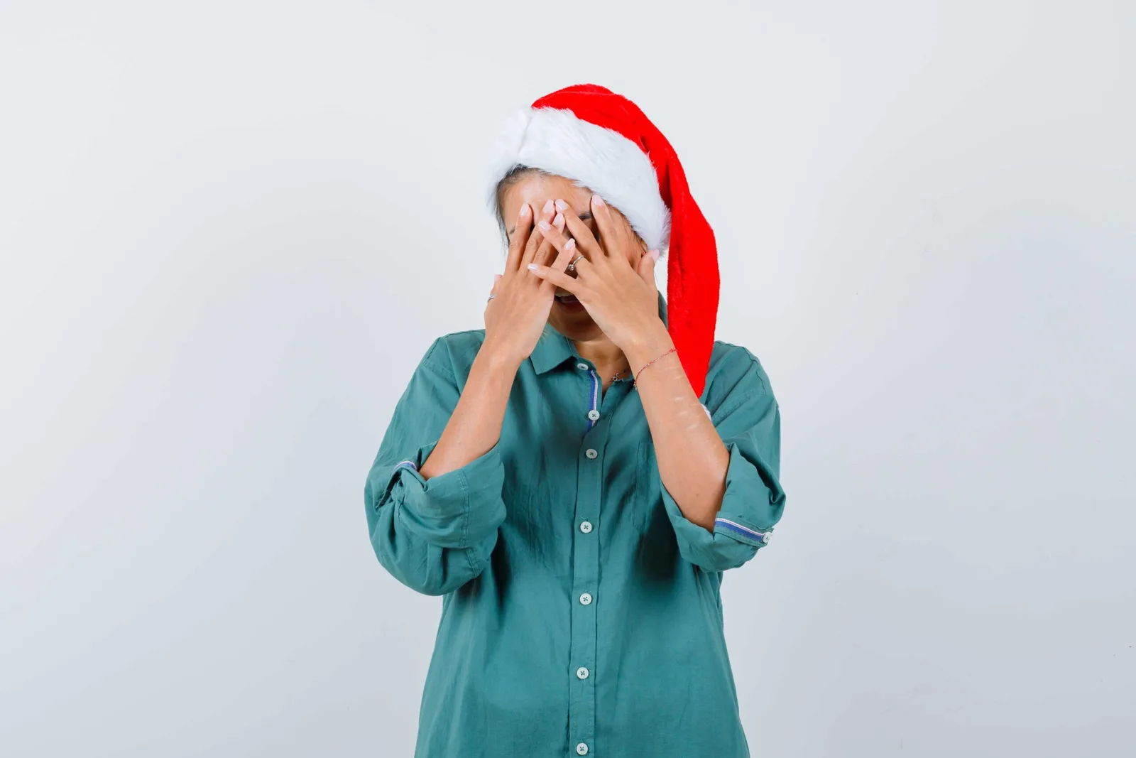 Mulher com gorro de Natal cobrindo o rosto por estresse, representando ansiedade durante o fim de ano.