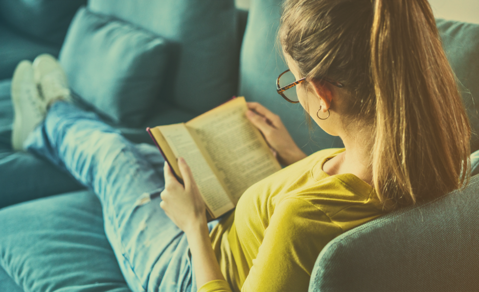 Mulher lendo um livro sentada no sofá.