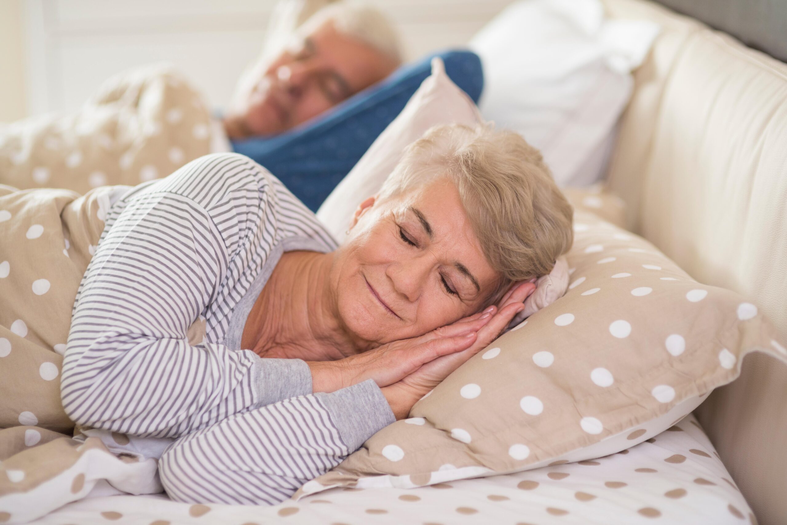 Casal idoso dormindo tranquilamente em cama confortável, representando sono de qualidade e equilíbrio emocional.